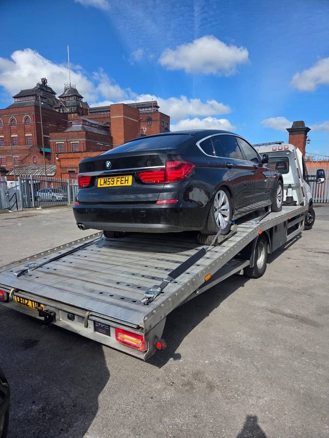Black BMW sedan loaded on recovery truck flatbed with city backdrop