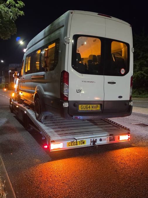 White Ford Transit van transported on recovery truck at night