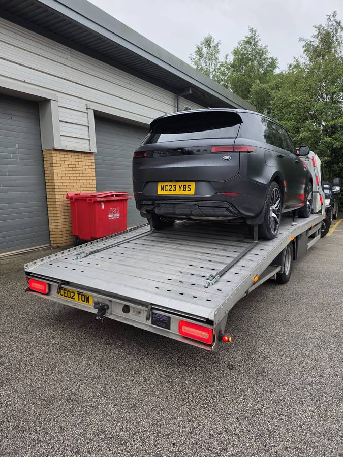 Black Ford electric vehicle on recovery flatbed at residential house driveway