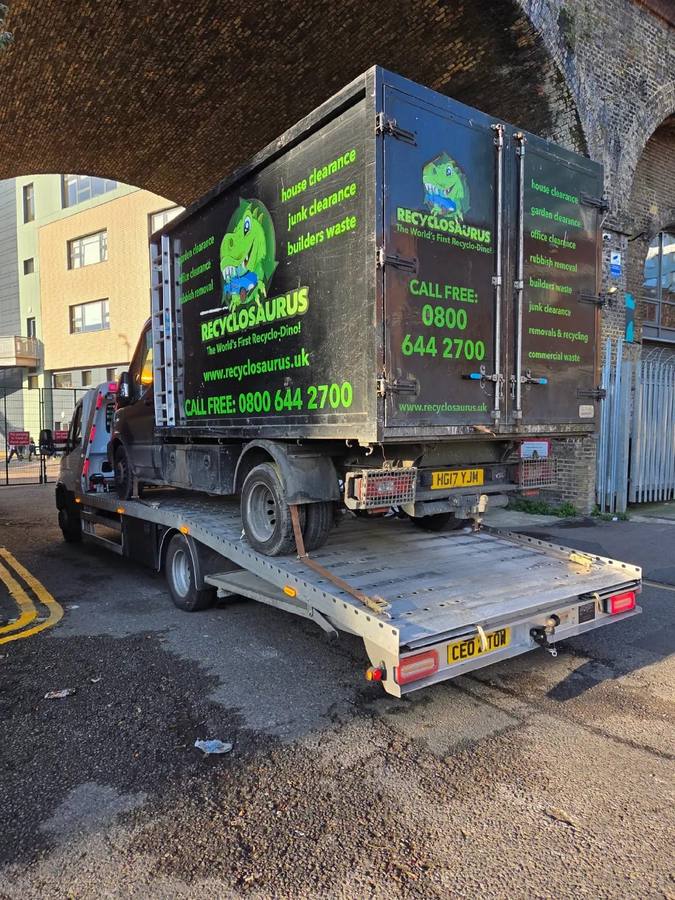 Dark Recyclosauras branded waste truck on recovery flatbed at urban location