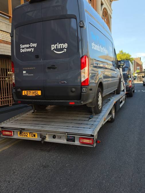 Black Amazon Prime delivery van secured on recovery flatbed in street